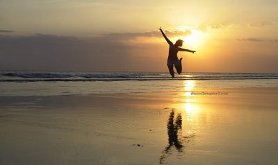 image of woman jumping for joy on beach at sunset