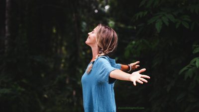 Smiling woman in forest with arms outstretched for how to get negative thoughts out of your mind blog page