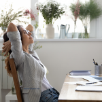 woman leaning back at her desk closing her eyes to breath and reduce stress and anxiety by staying present